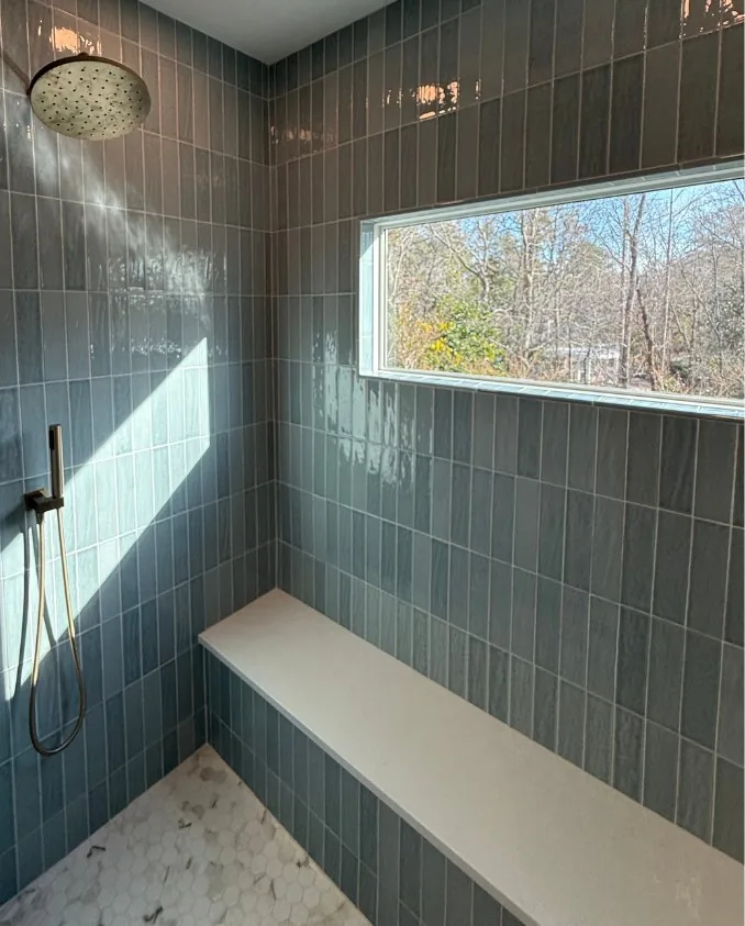A tiled walk-in shower with a bench and a freestanding tub beyond