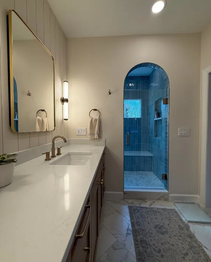 A double vanity with stone countertop, arched mirrors and wall sconces