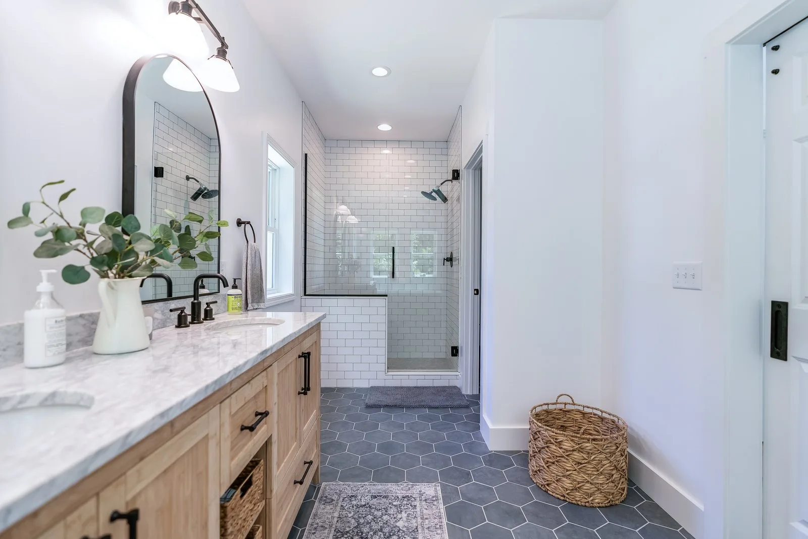 A primary bathroom with a white oak vanity, arched mirror and walk-in tile shower