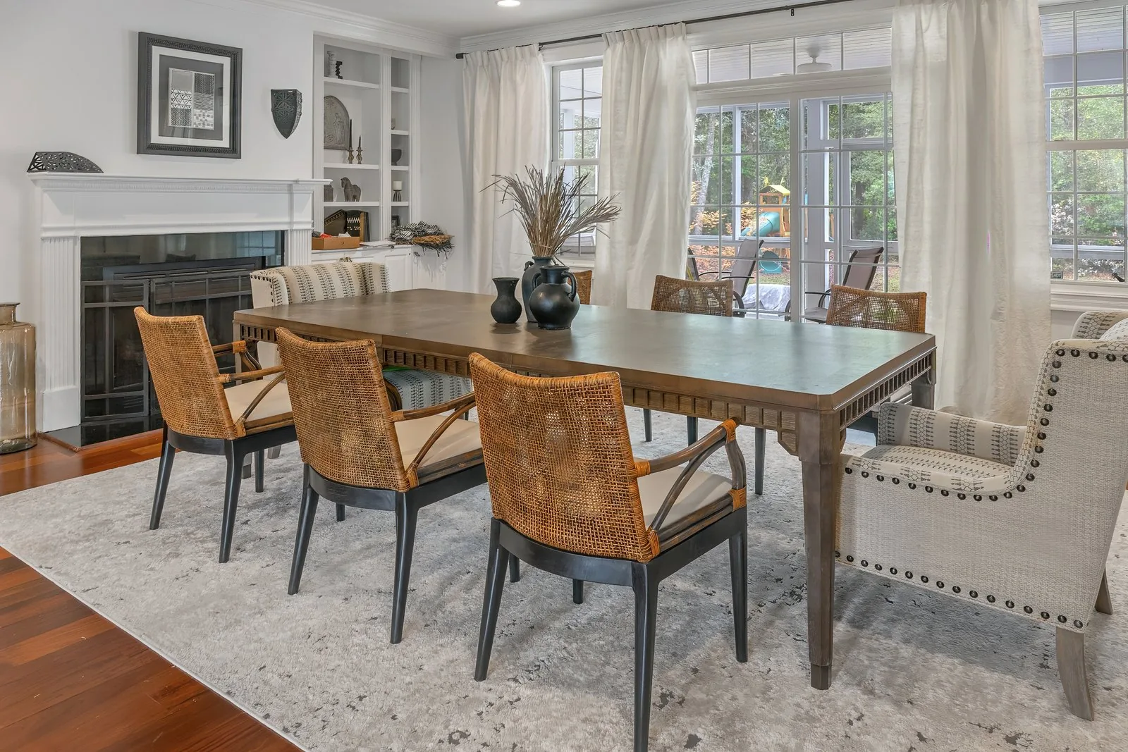 A dining room with a fireplace, built-in shelving and woven dining chairs