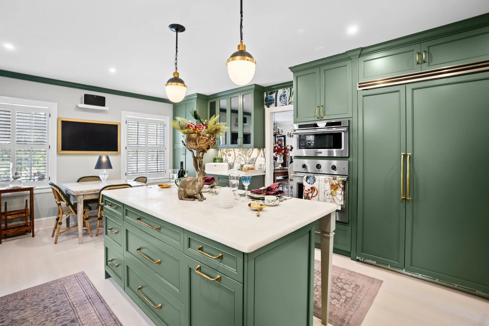 A kitchen with deep green cabinetry, brass hardware and a stone island
