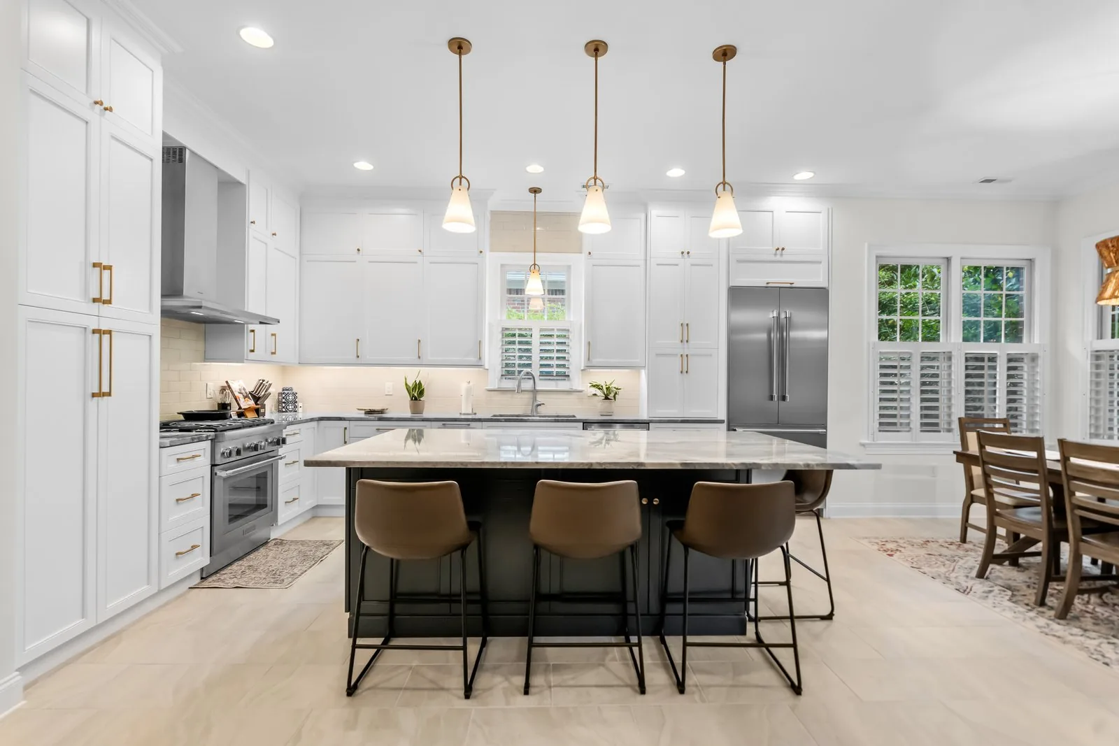 A white kitchen with a dark island, brass pendants and panelled appliances